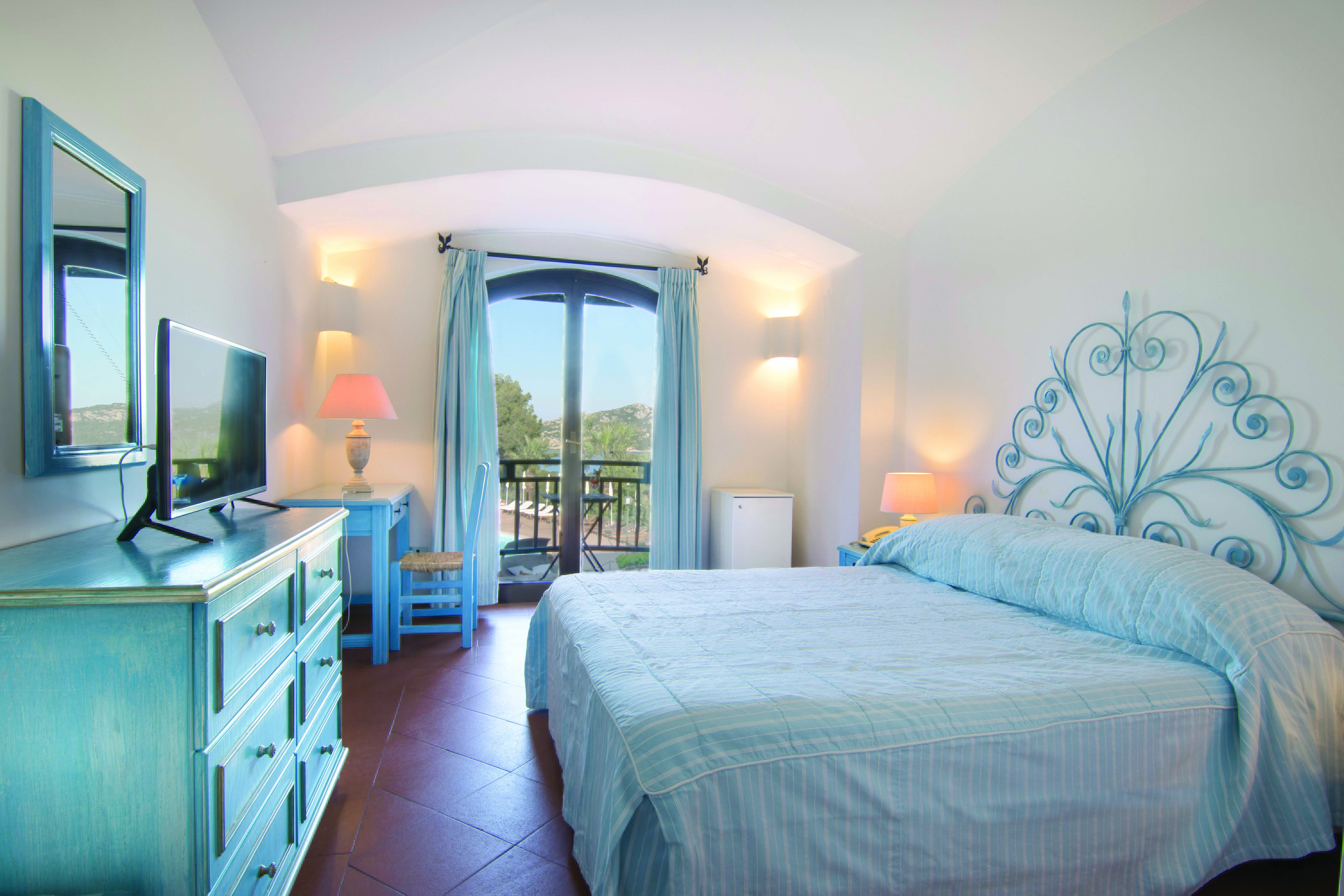 Hotel Le Ginestre Sardinia guestroom, double bed, chest of drawers, doors leading to balcony with garden view