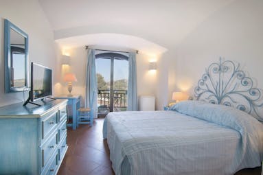 Hotel Le Ginestre Sardinia guestroom, double bed, chest of drawers, doors leading to balcony with garden view