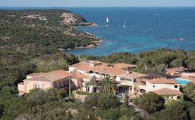 Hotel Le Ginestre Sardinia resort, hotel buildings nestled on wooded coastline, sea and beach in background