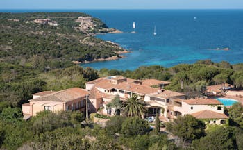 Hotel Le Ginestre Sardinia resort, hotel buildings nestled on wooded coastline, sea and beach in background