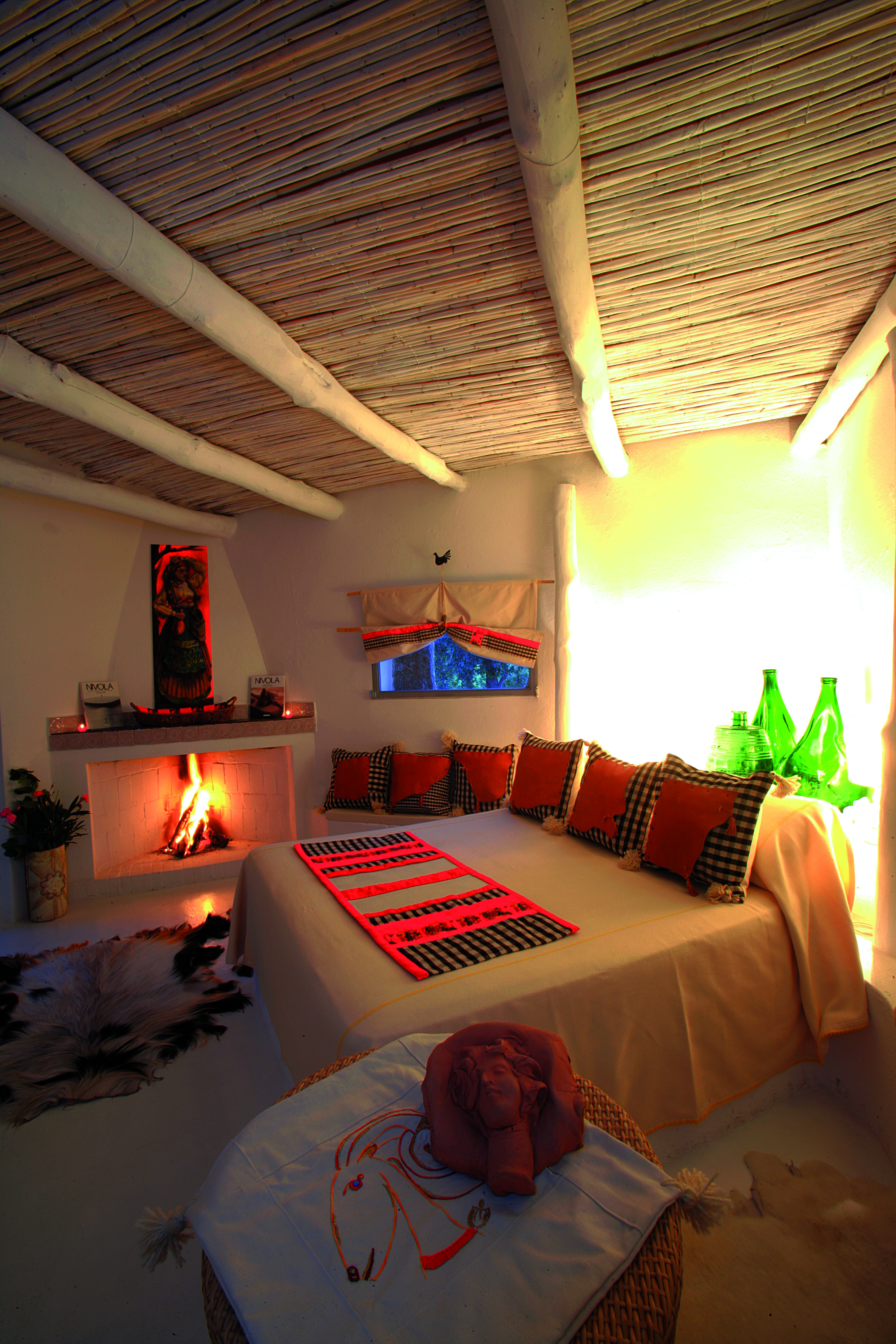 Hotel Su Gologone bedroom with large bed, a fireplace, table and small window 