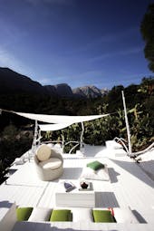Hotel Su Gologone white painted rooftop terrace with seating areas, green cushions and a white hammock looking over mountains