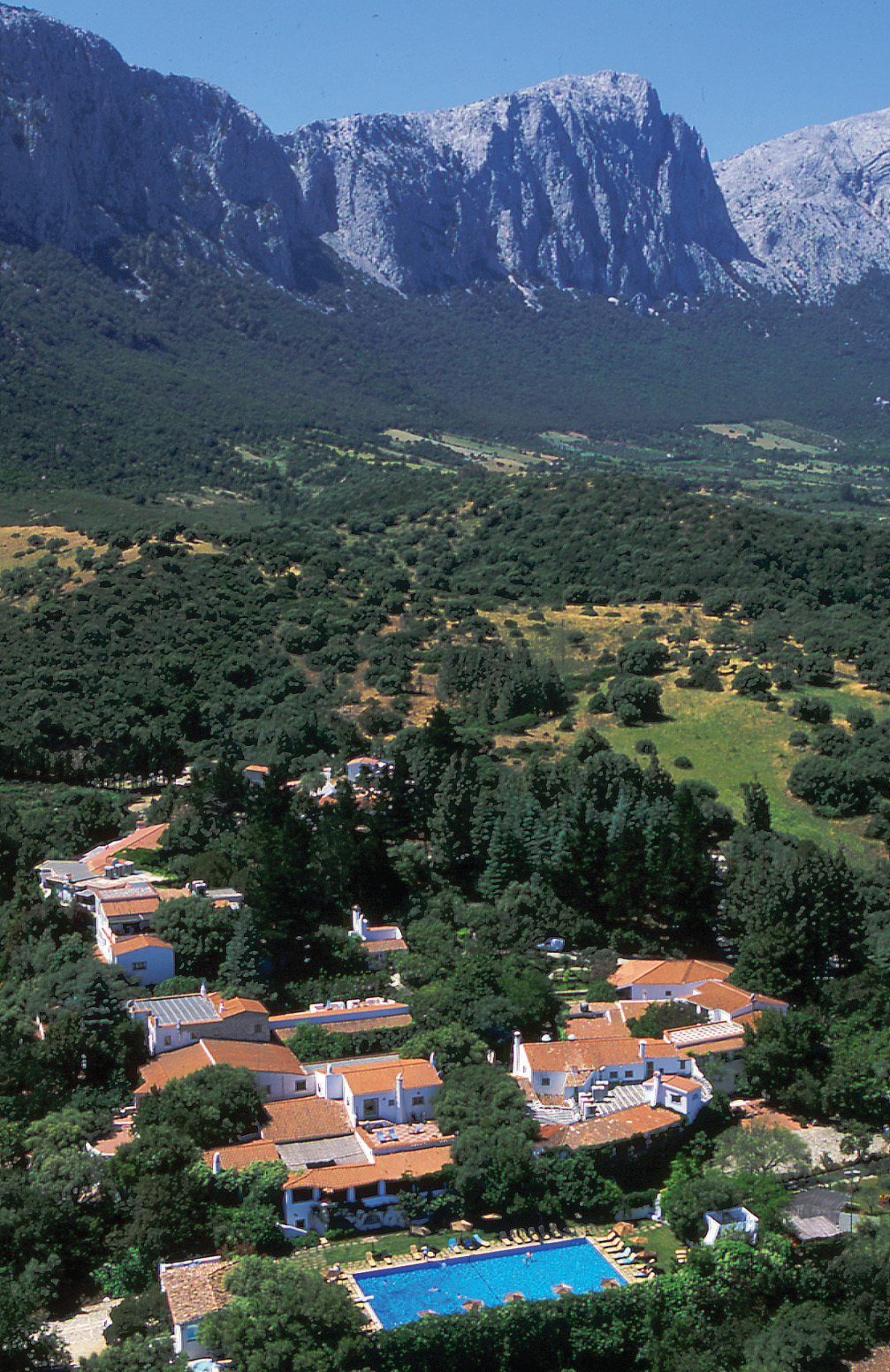 Aerial view of hotel shown below large mountain range and surrounded by greenery