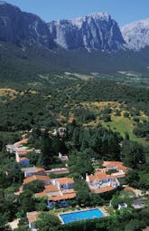 Aerial view of hotel shown below large mountain range and surrounded by greenery