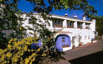 Exterior of hotel with white building, trees around the sides and purple door