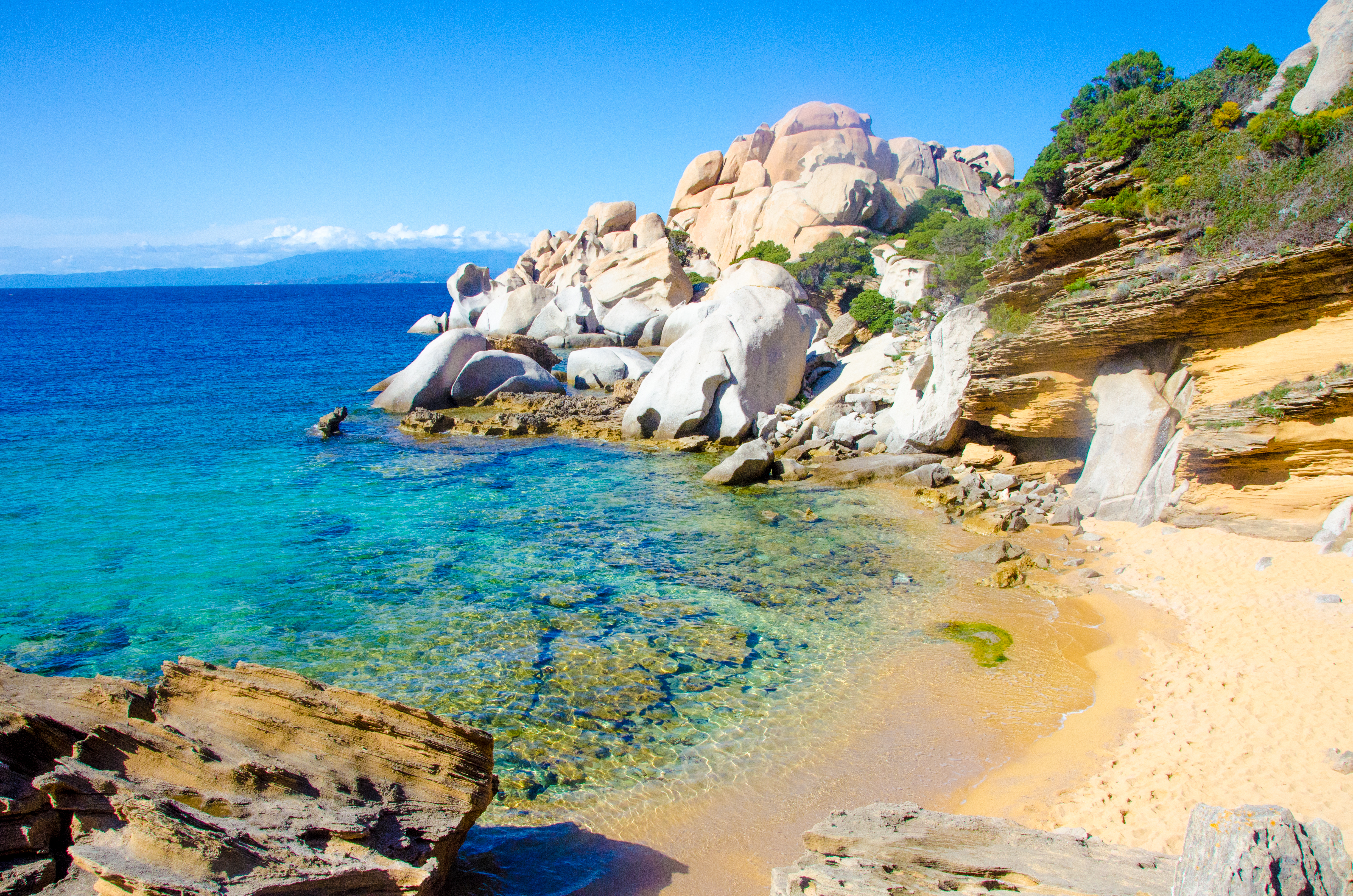 Emeral sea and yellow sand beach with rocks either side of cove in Sardinia