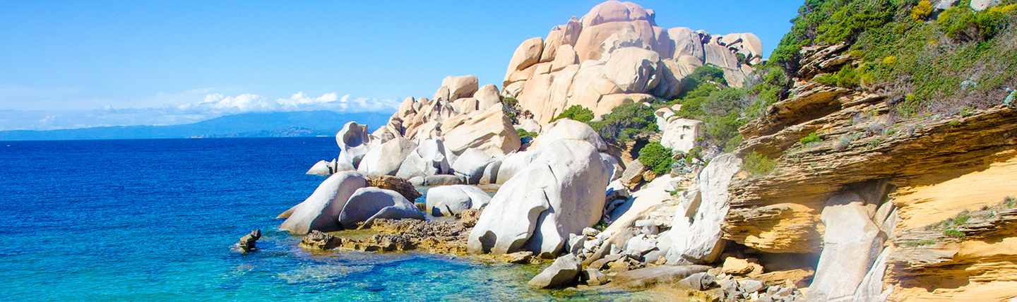 White and orange tinged craggy cliffs dropping into blue sea in Sardinia