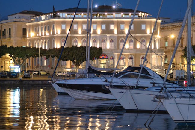 Exterior of hotel from the sea looking out over the boats at night with hotel lights lit up 