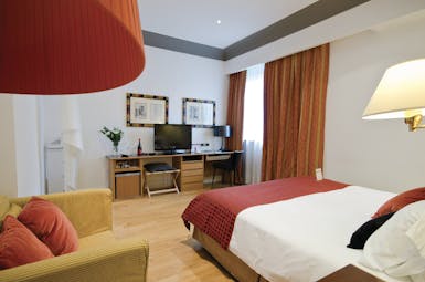 Deluxe double room with a red and white colour scheme, a large double bed, television and armcahir