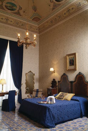 Bedroom with high ceilings, a chandelier, double bed with blue throw and mirror