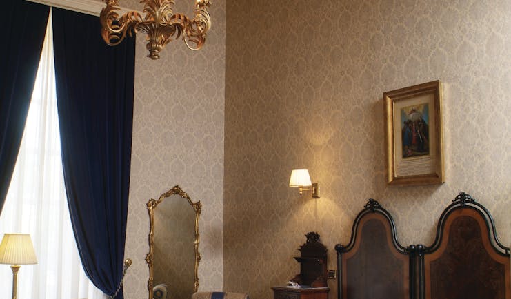 Bedroom with high ceilings, a chandelier, double bed with blue throw and mirror