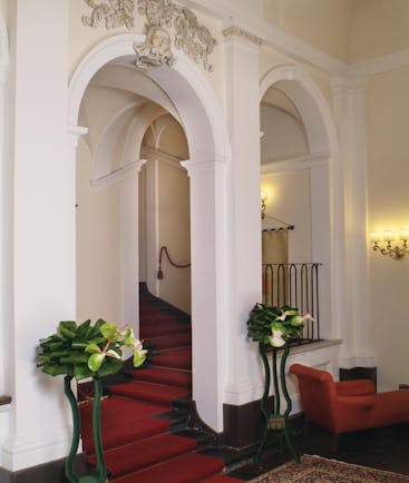 Hallways area with red carpet, white arching pillars and potted plants