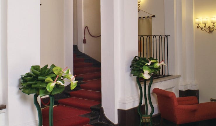 Hallways area with red carpet, white arching pillars and potted plants