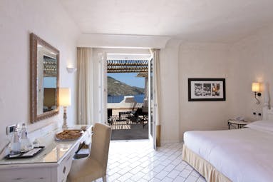 Deluxe suite at the Therasia Resort with a white colour scheme, large white double bed, and double doors opening onto a terrace balcony 