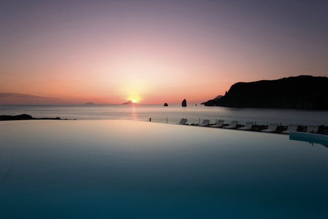 View of a pink sunset setting over the sea with the Therasia resort swimming pool in front 