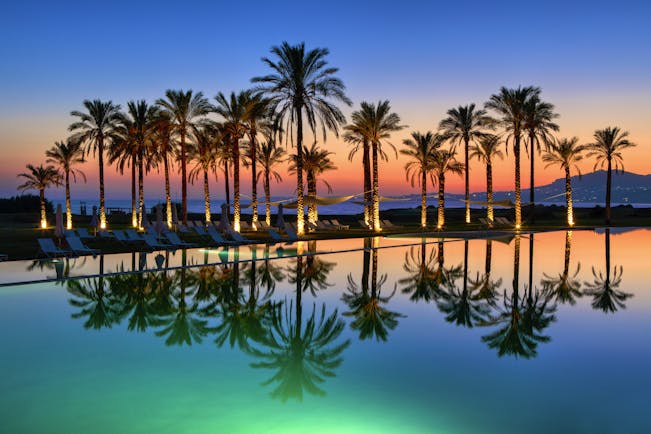 Verdura Resort evening with palm trees and swimming pool reflections