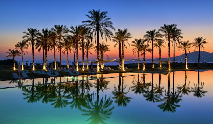 Verdura Resort evening with palm trees and swimming pool reflections
