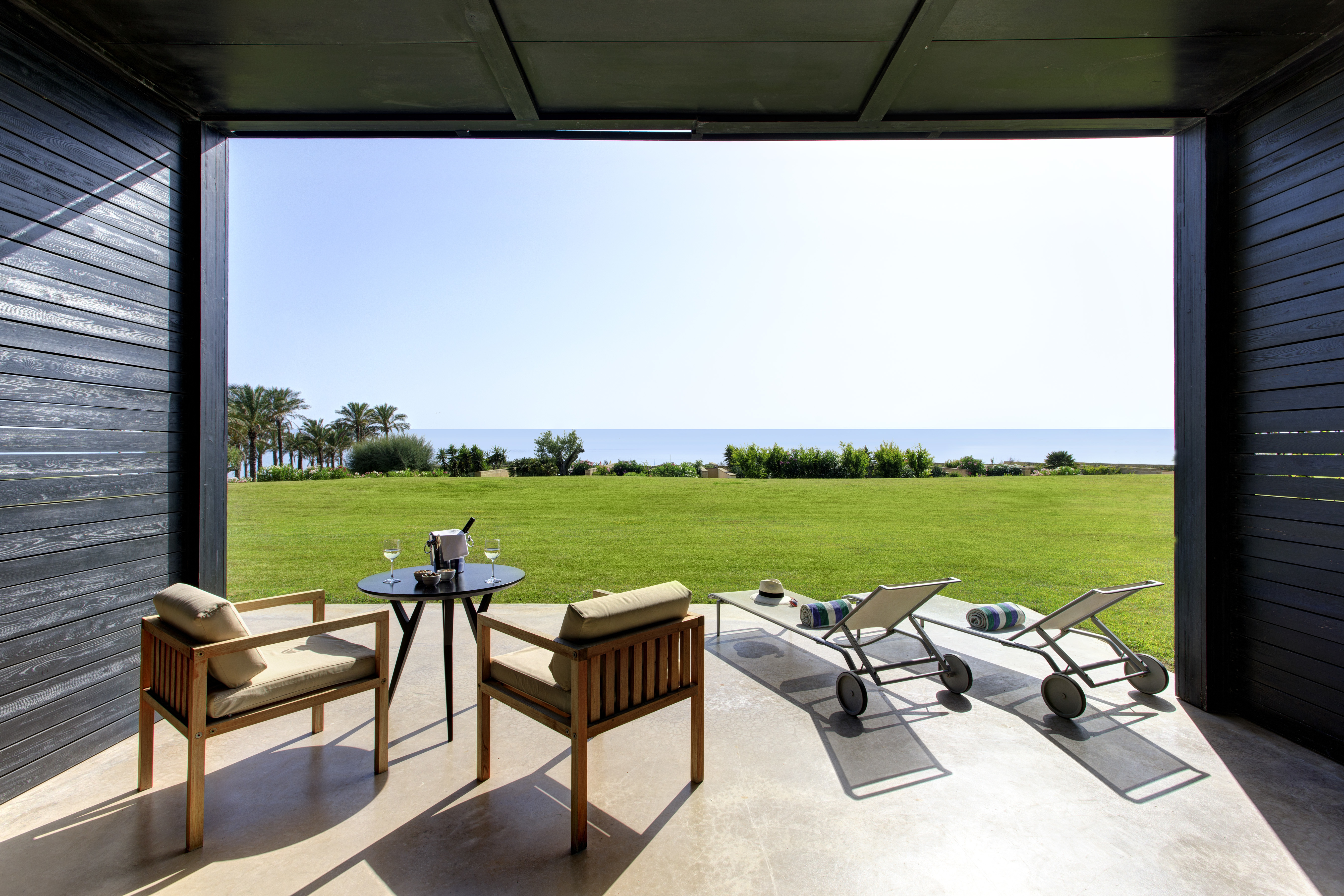 Verdura Resort room with chairs and sunloungers overlooking grass and sea