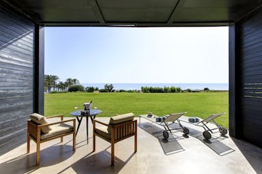 Verdura Resort room with chairs and sunloungers overlooking grass and sea