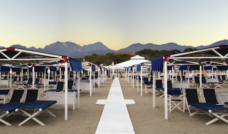 Beach with blue sunloungers and deck chairs on the sand and mountain peaks in the background