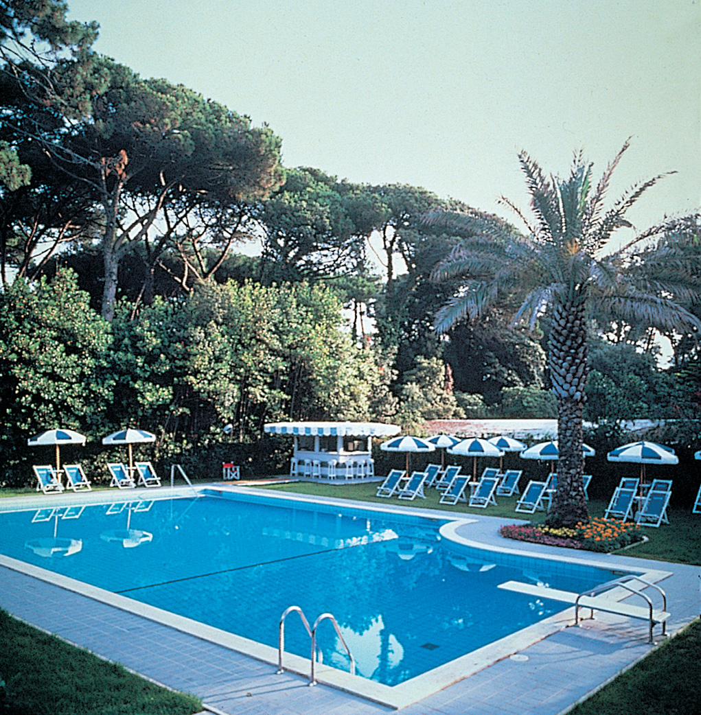 Outdoor swimming pool with palm trees around and blue and white deck chairs and umbrellas