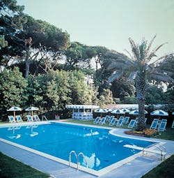 Outdoor swimming pool with palm trees around and blue and white deck chairs and umbrellas