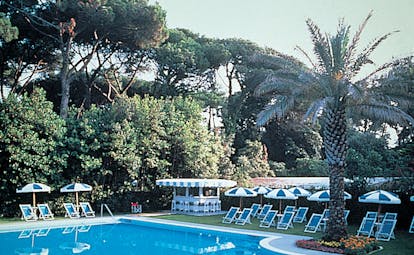Outdoor swimming pool with palm trees around and blue and white deck chairs and umbrellas