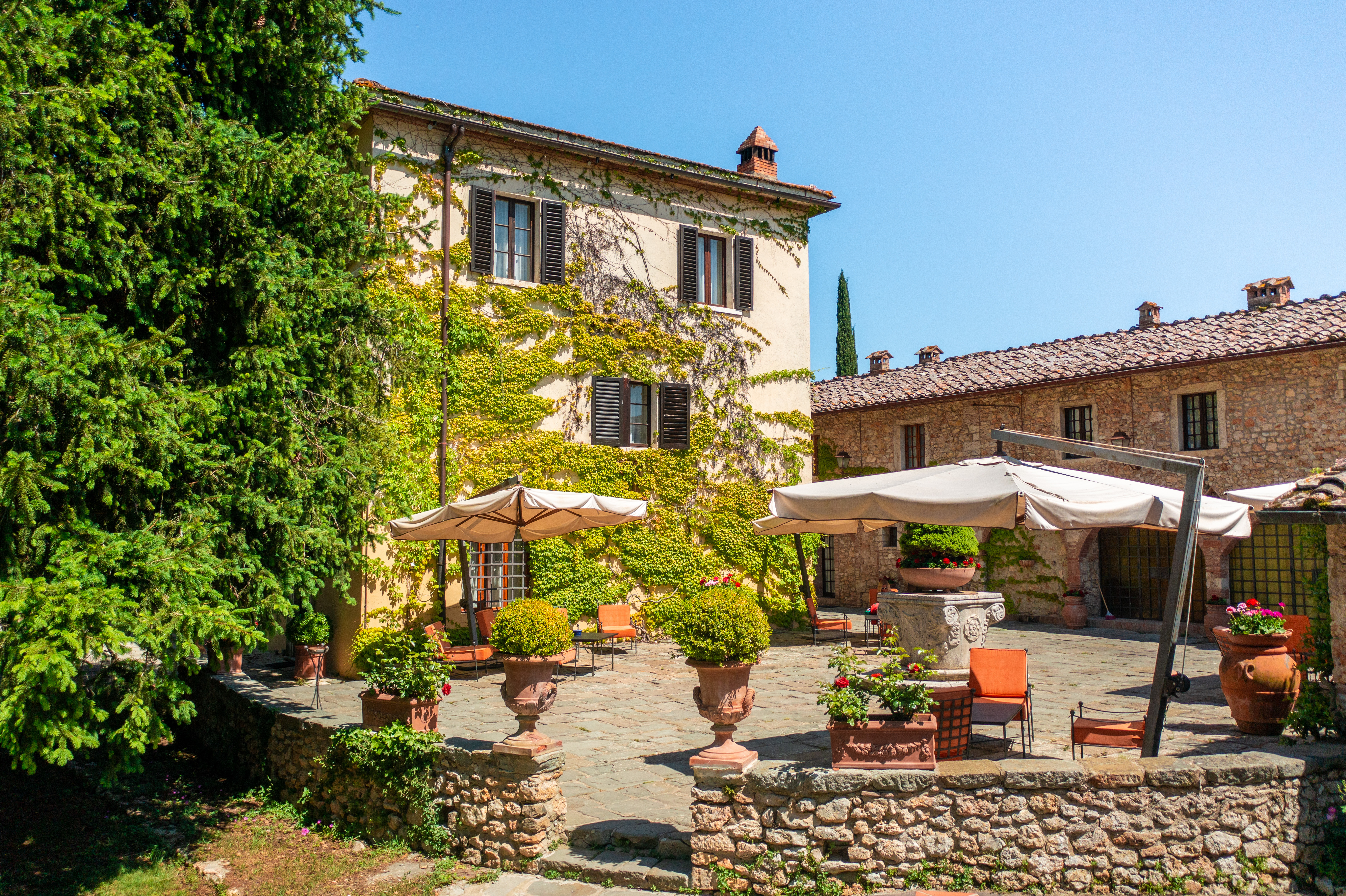 Borgo San Luigi seen from the outside, with traditional Tuscan facade, climbing vines, and cobbled courtyard with parasols and chairs