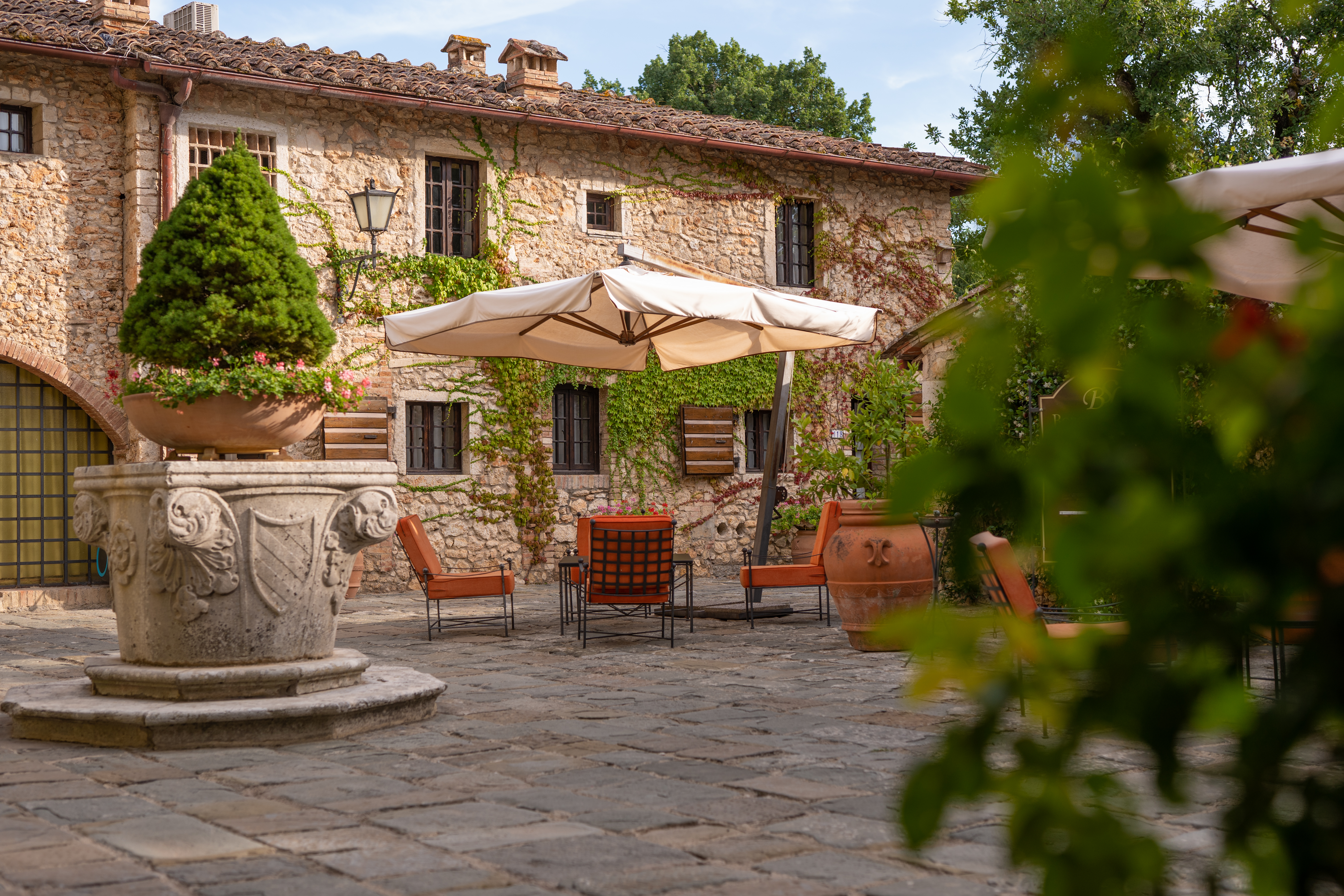 Borgo San Luigi courtyard area, with red and black iron chairs, a parasol, and ornate planter with the hotel's traditional stone building in the background