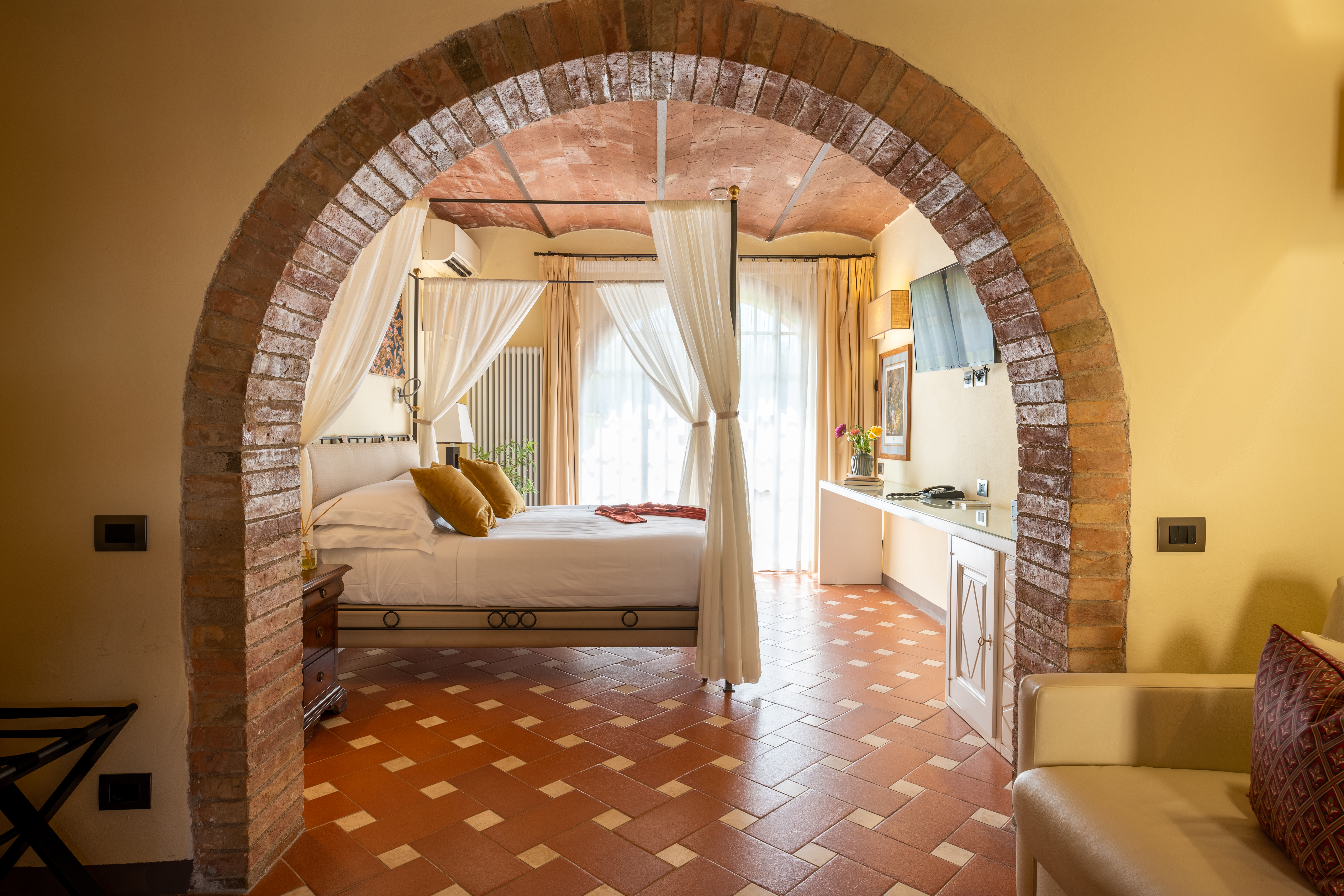 Borgo San Luigi Deluxe Terrace Room with stone arch leading towards a canopy bed and double doors beyond