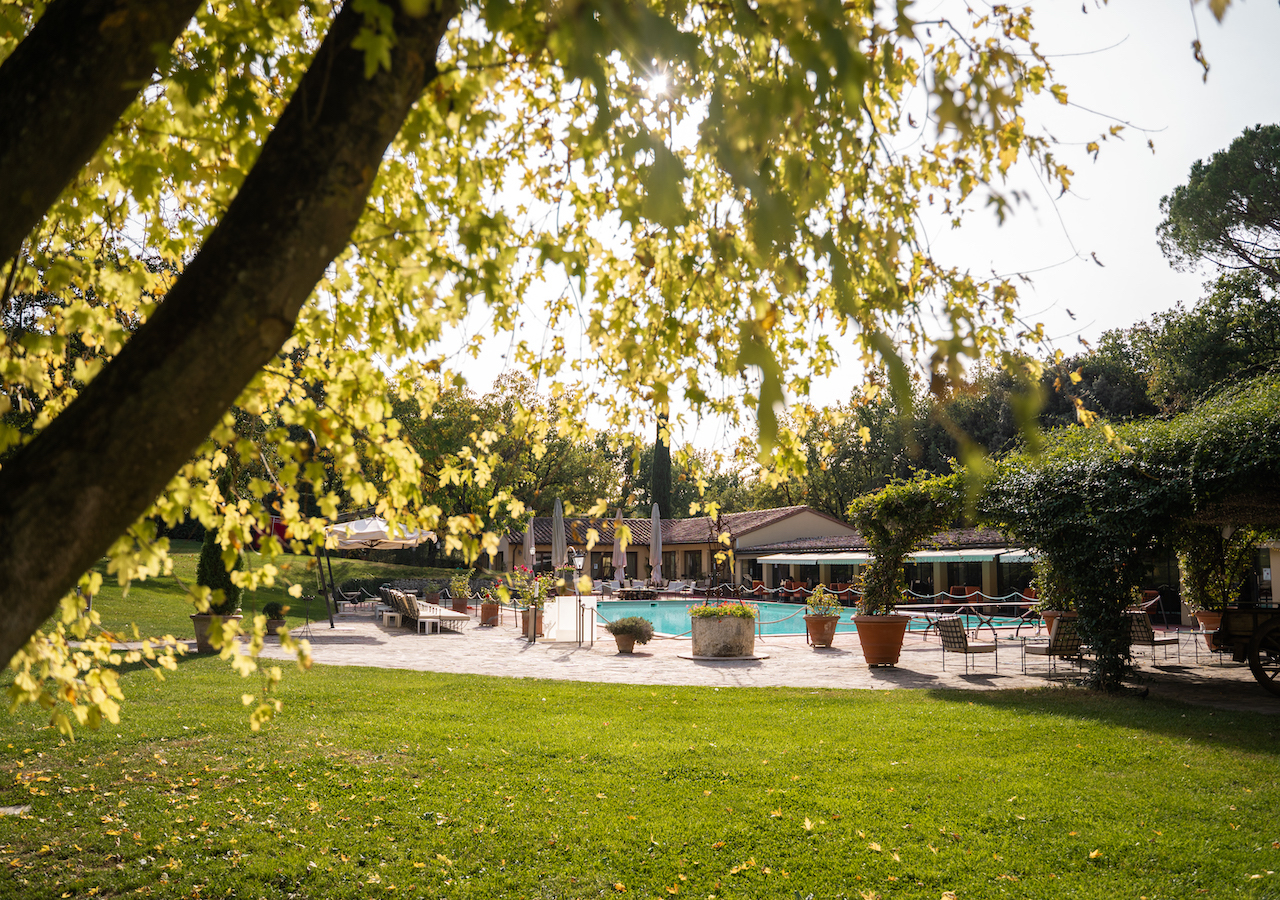 Borgo San Luigi lawn shaded under many trees, with the poolside and pool bar in the distance