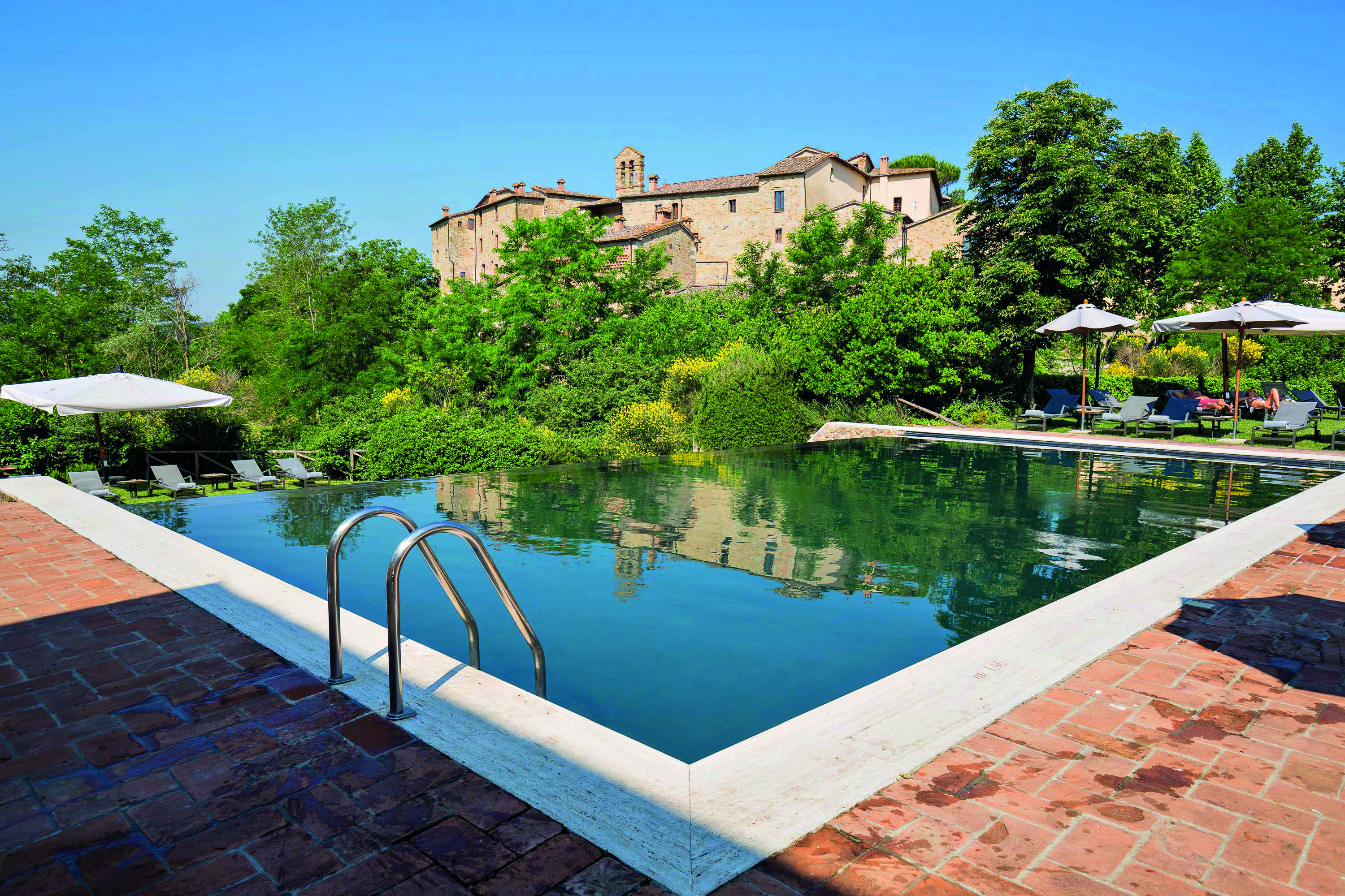 Castel Monastero Tuscany infinity pool sun loungers umbrellas