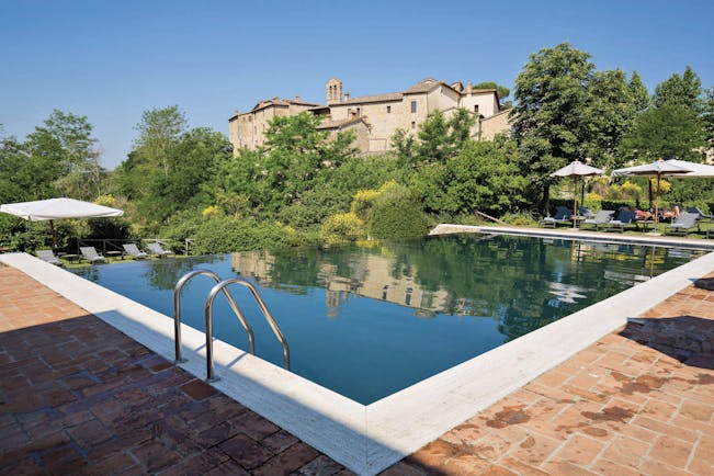 Castel Monastero Tuscany infinity pool sun loungers umbrellas