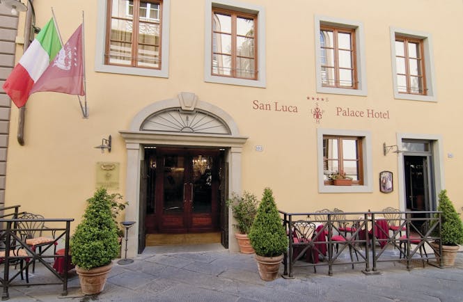 Exterior view of the entrance to the hotel with the Italian flag hanging outside and potted plants