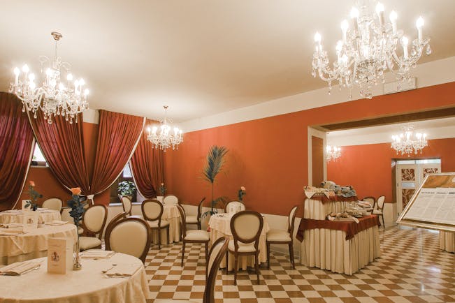 Restaurant with large chandeliers hanging from the ceiling, circular tables laid out around the room and a buffet spread in the corner