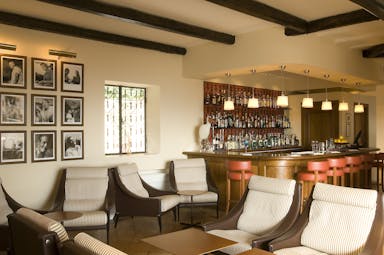 Indoor bar with photos on the wall, cushioned seats and a wood pannelled bar area with drinks behind