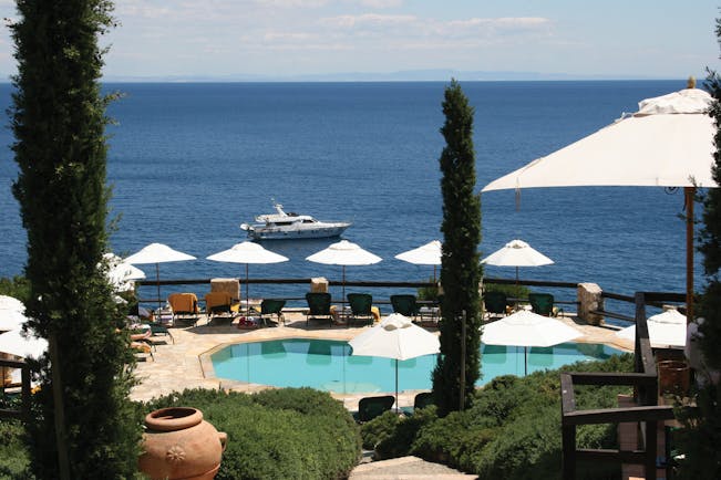 Pool and sea view with bushes and sunloungers and a boat in the sea