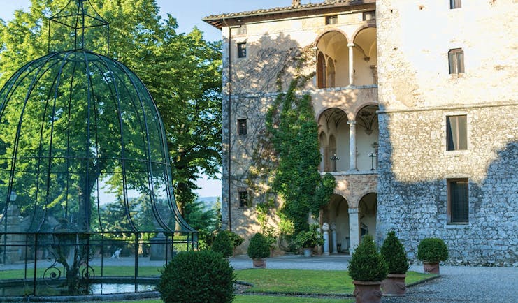View of the exterior of the Relais La Suvera with a stone building with arched window and greenery outside