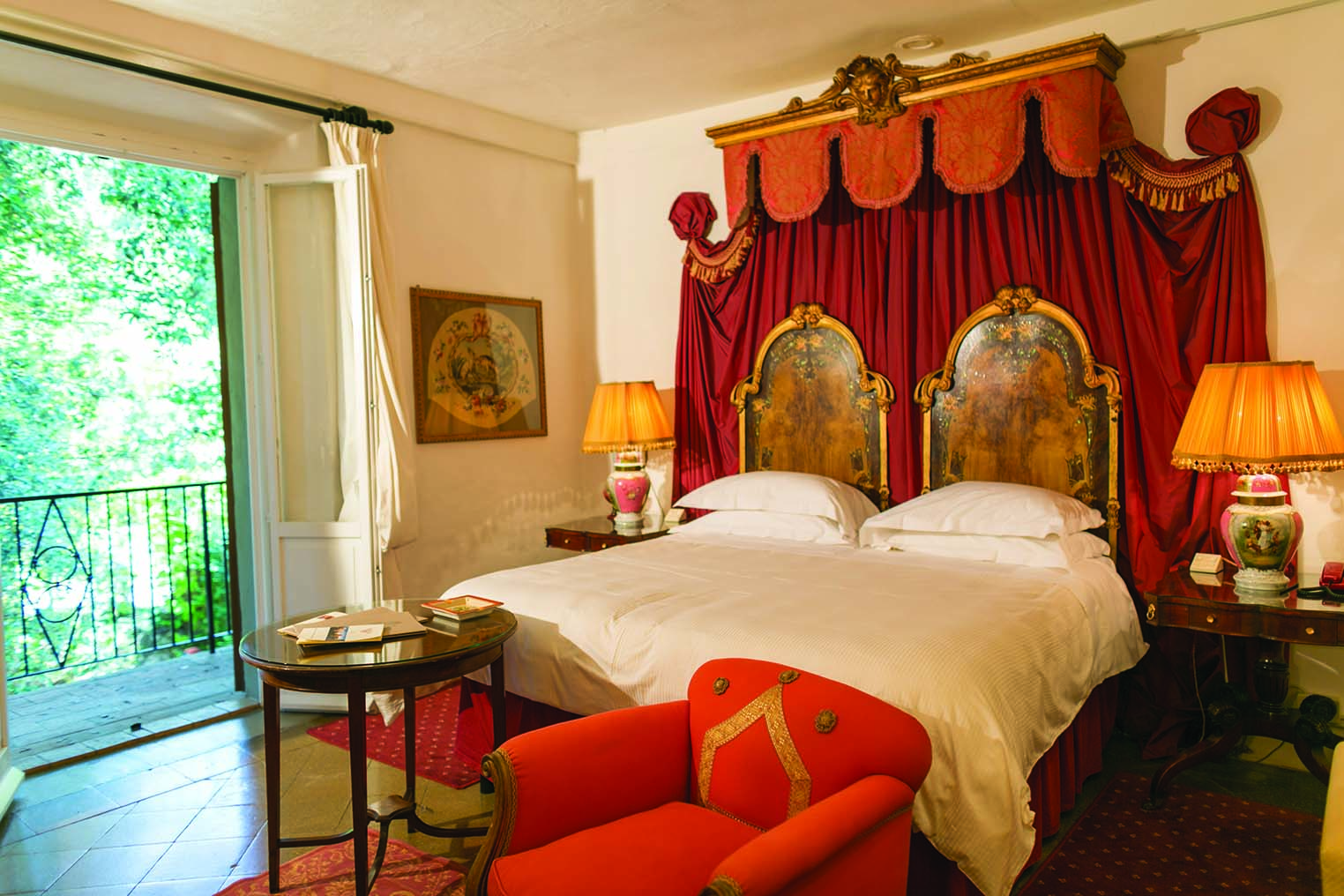 Farmhouse room at the Relais la Suvera with a large double bed, red armchair and double doors opening onto a balcony