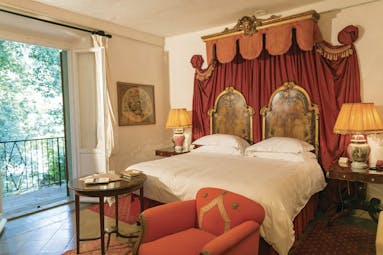 Farmhouse room at the Relais la Suvera with a large double bed, red armchair and double doors opening onto a balcony