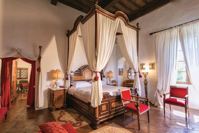 Fox suite at the Relais la Suvera with a large wooden bed with white drapes, a white and red colour scheme with red chairs around the room 