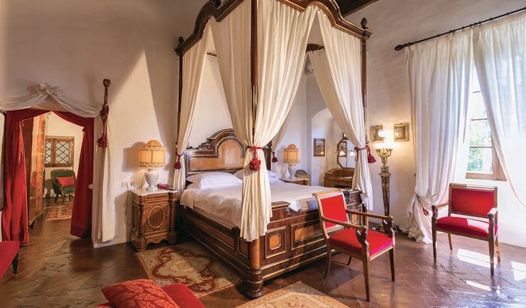 Fox suite at the Relais la Suvera with a large wooden bed with white drapes, a white and red colour scheme with red chairs around the room 