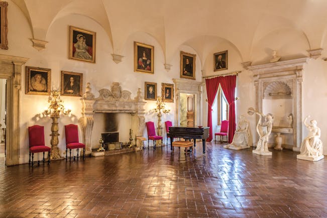 Large hall at the Relais la Suvera with gold framed paintings around the walls, red chairs and statutes around the edges of the room 