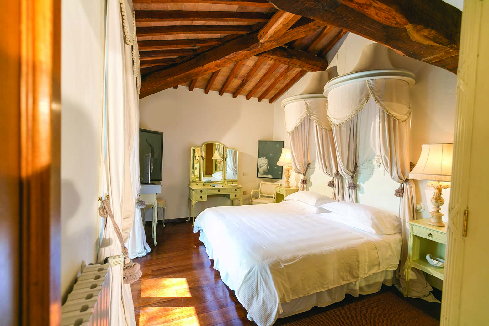 Junior suite in the Relais la Suvera with white and cream decorations with a wooden ceiling, large bed and vanity mirror