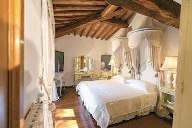 Junior suite in the Relais la Suvera with white and cream decorations with a wooden ceiling, large bed and vanity mirror