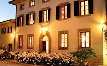 Exterior of hotel with white flowers infront, shutters on windows and wall lamps glowing