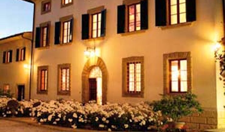 Exterior of hotel with white flowers infront, shutters on windows and wall lamps glowing