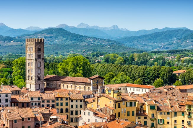 Aerial view of the terracotta roofs of buildings in medieval Lucca with green hills in the distance