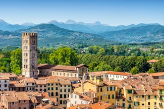 Aerial view of the terracotta roofs of buildings in medieval Lucca with green hills in the distance