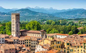 Aerial view of the terracotta roofs of buildings in medieval Lucca with green hills in the distance